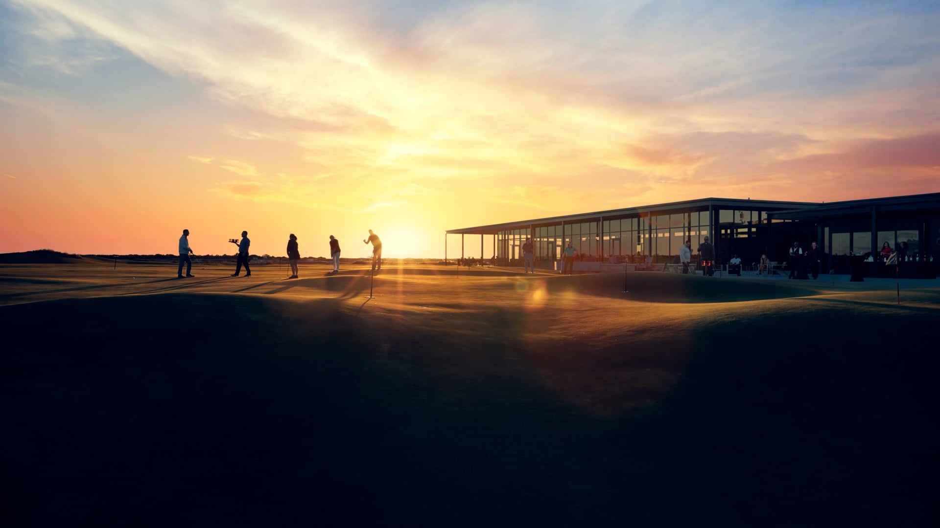 Golfers putting beside the glass clubhouse at Streamsong as the sun sets